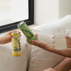 Two cans of Melo sparkling water and a glass of water on a couch.