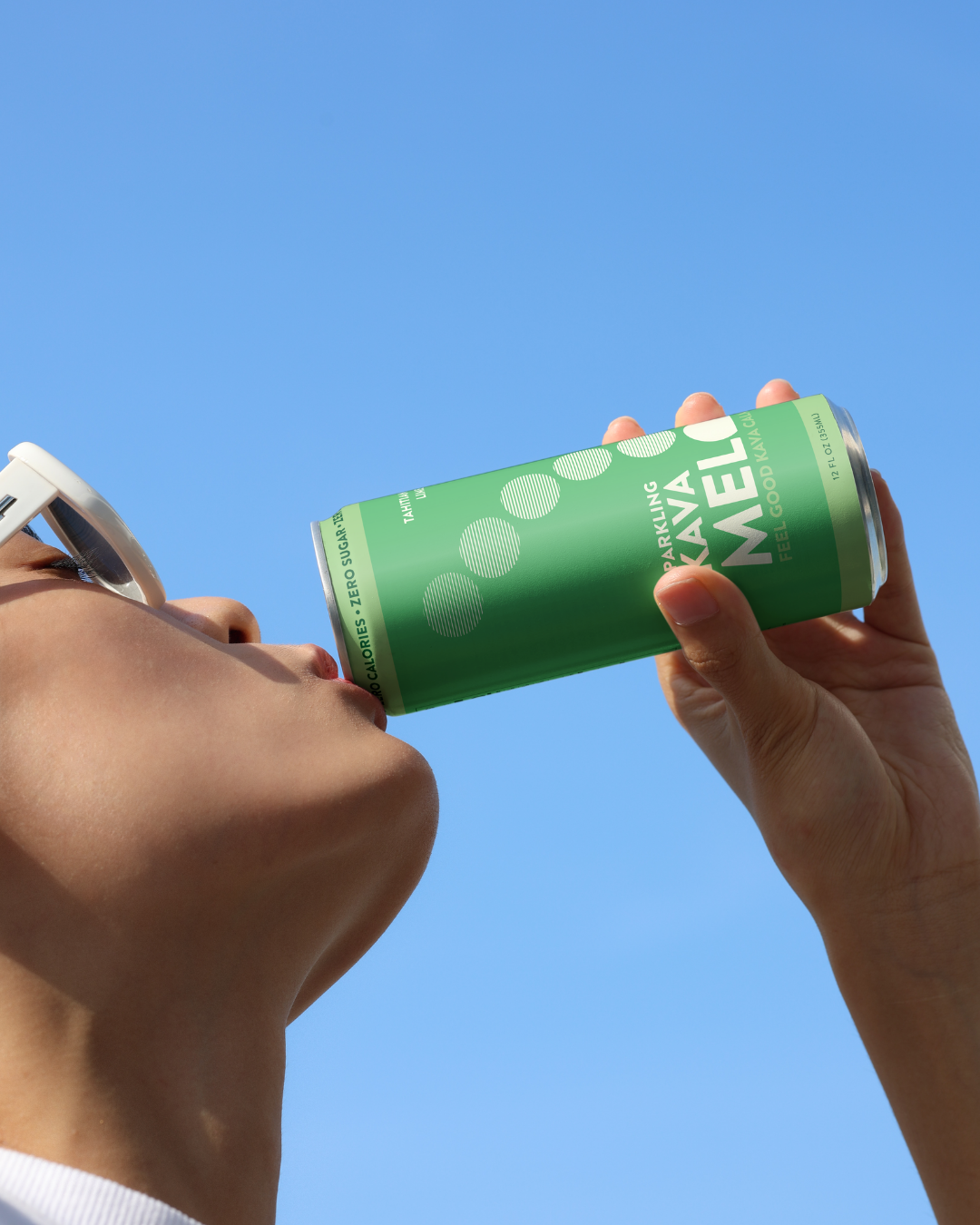 Person drinking from a green MELON energy drink can against a clear blue sky