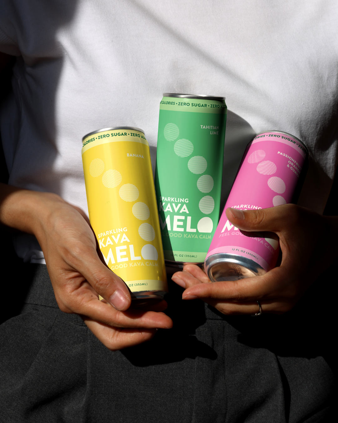 Three colorful cans held by a person against a white shirt background