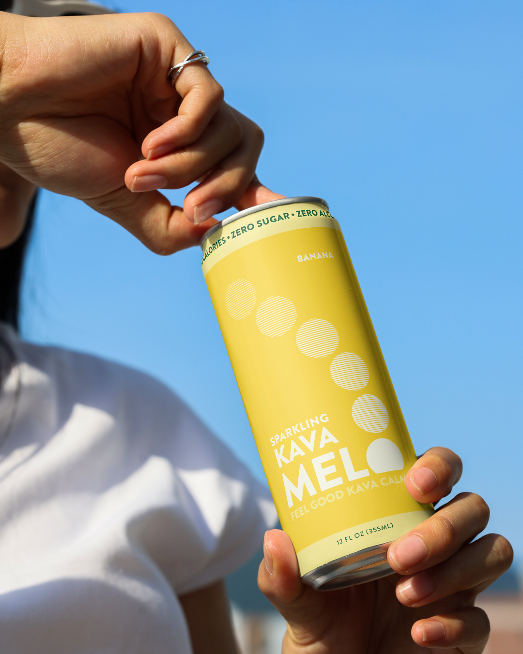 Person holding a yellow can of Kava Melo against a clear blue sky