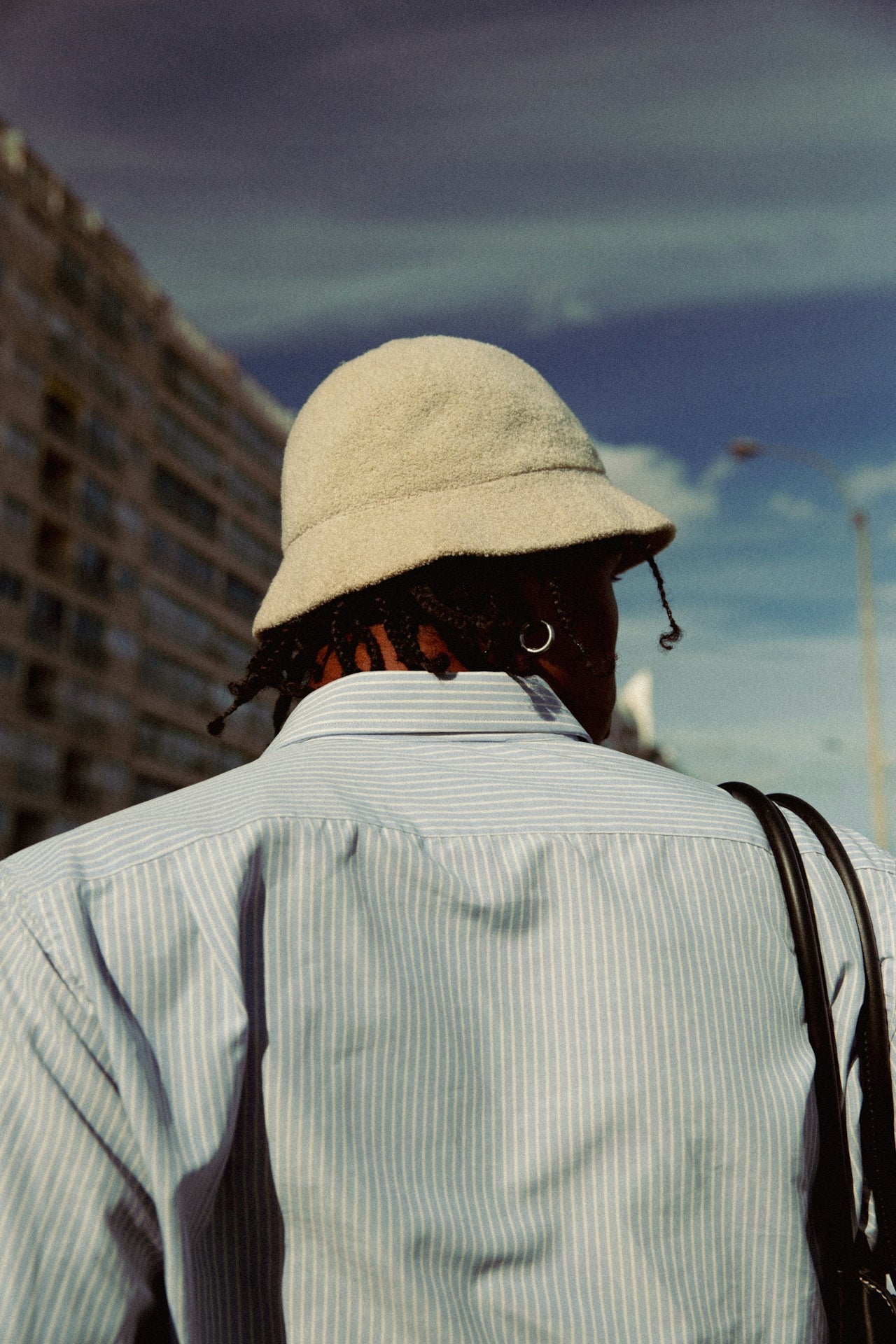 Person wearing a beige bucket hat and light-colored shirt with a blurred cityscape in the background