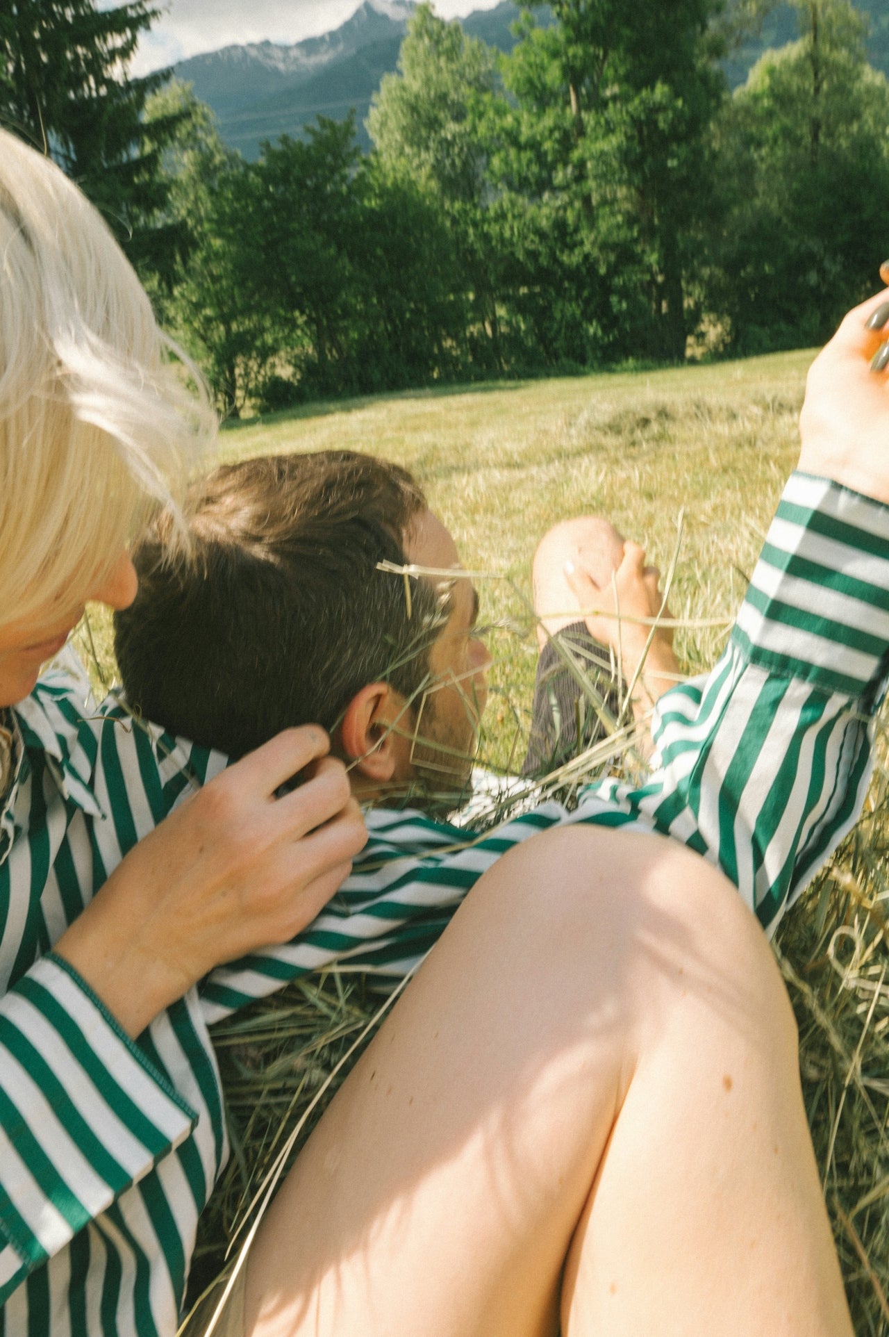 Two people sitting in a grassy field with mountains in the background
