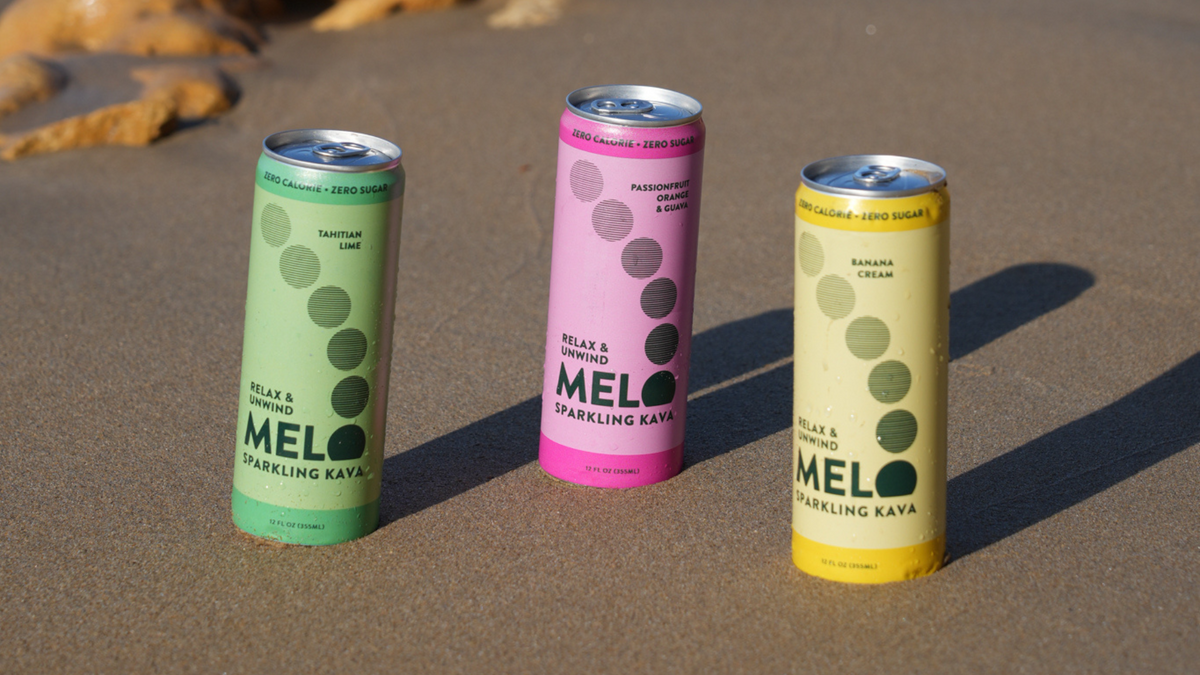 Three colorful cans of MEL sparkling raya on a sandy surface