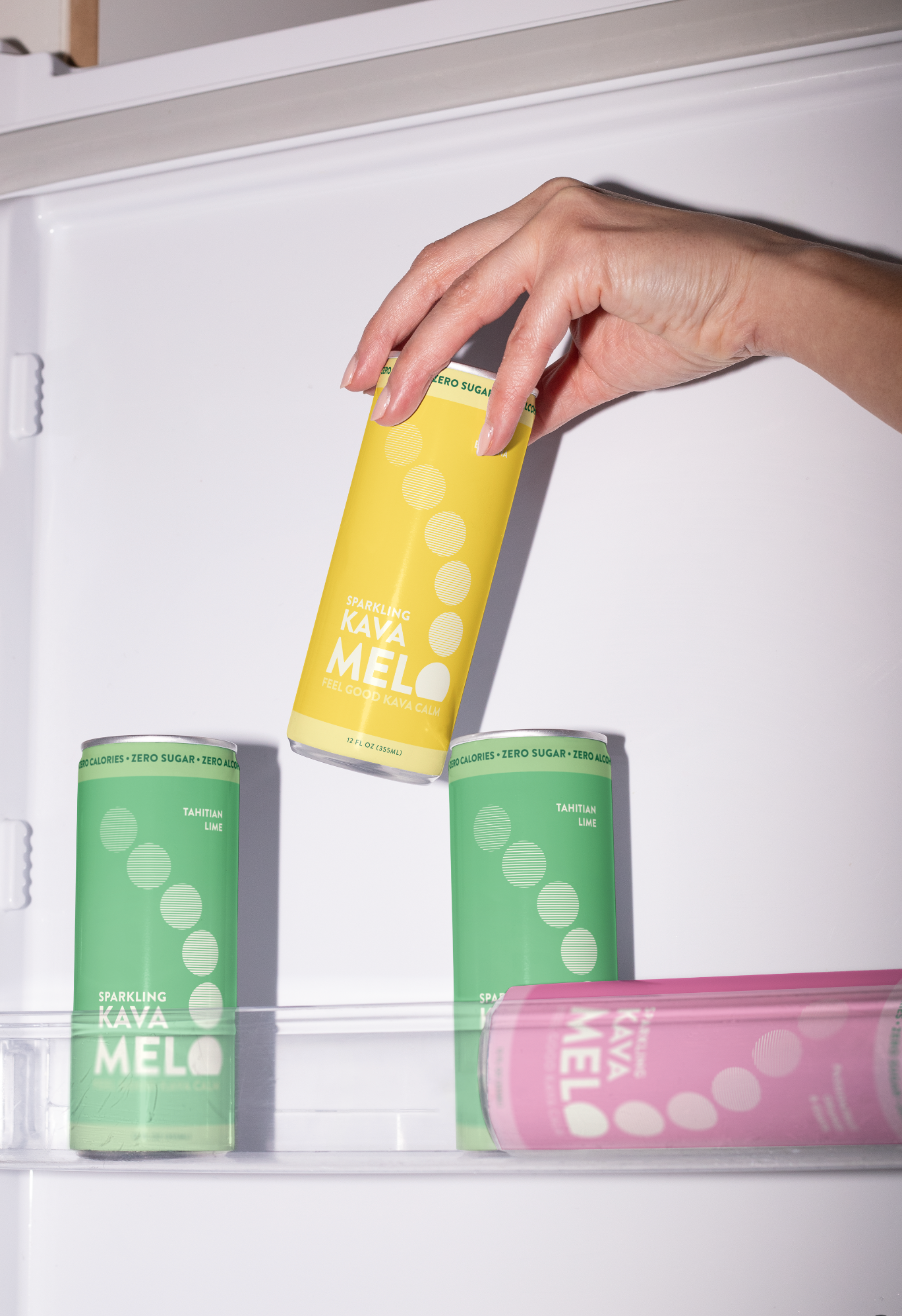 Hand reaching for a yellow can labeled 'Rava Mel' among other colorful cans in an open refrigerator.