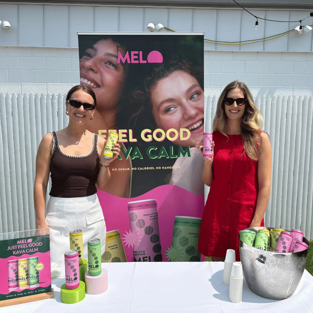 Two women holding Melo products in front of a promotional banner with the brand's logo and messaging.