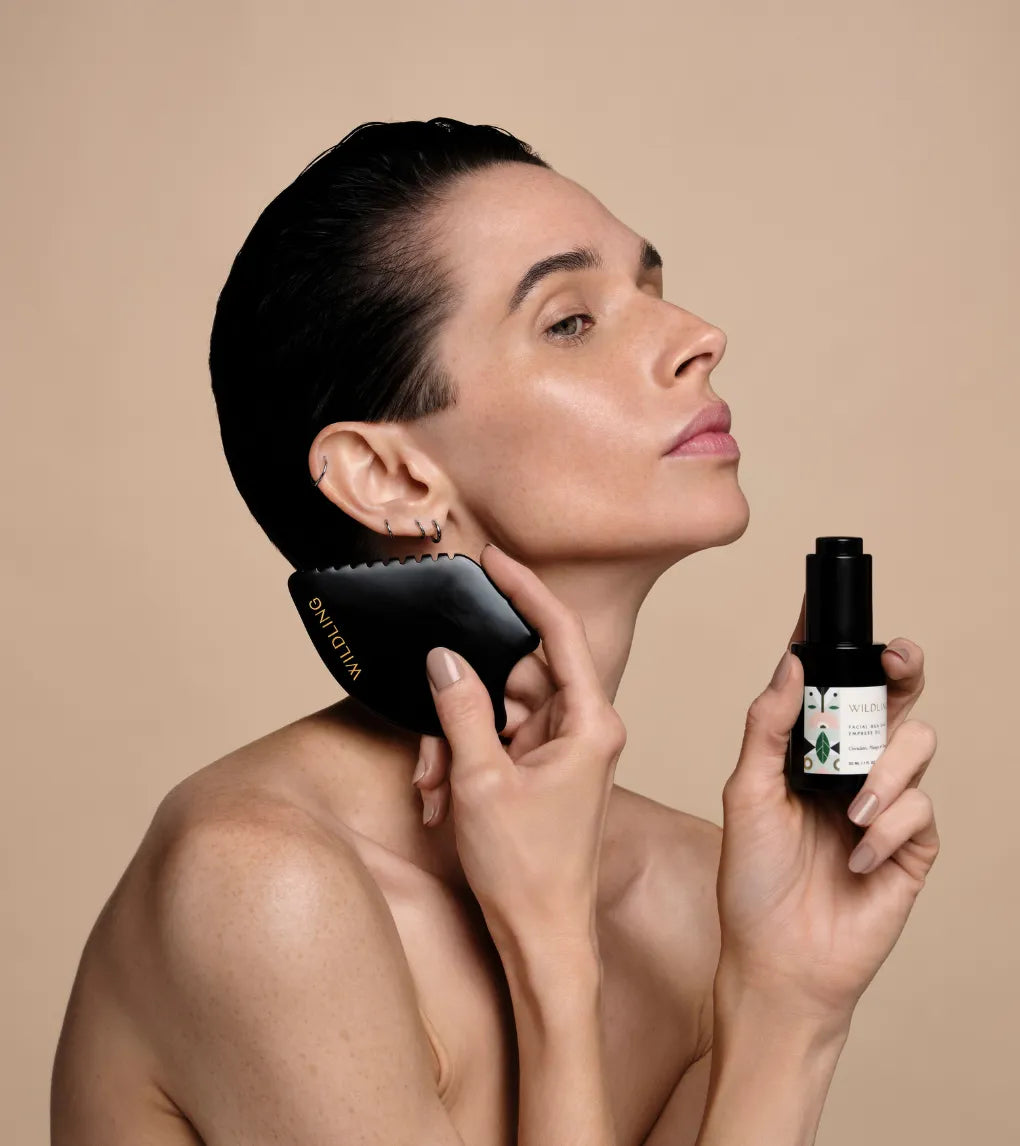 Woman using a black grooming tool and holding a bottle on a beige background