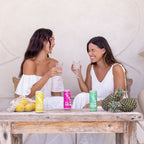 Two women sitting at a table with colorful drinks and pineapples.