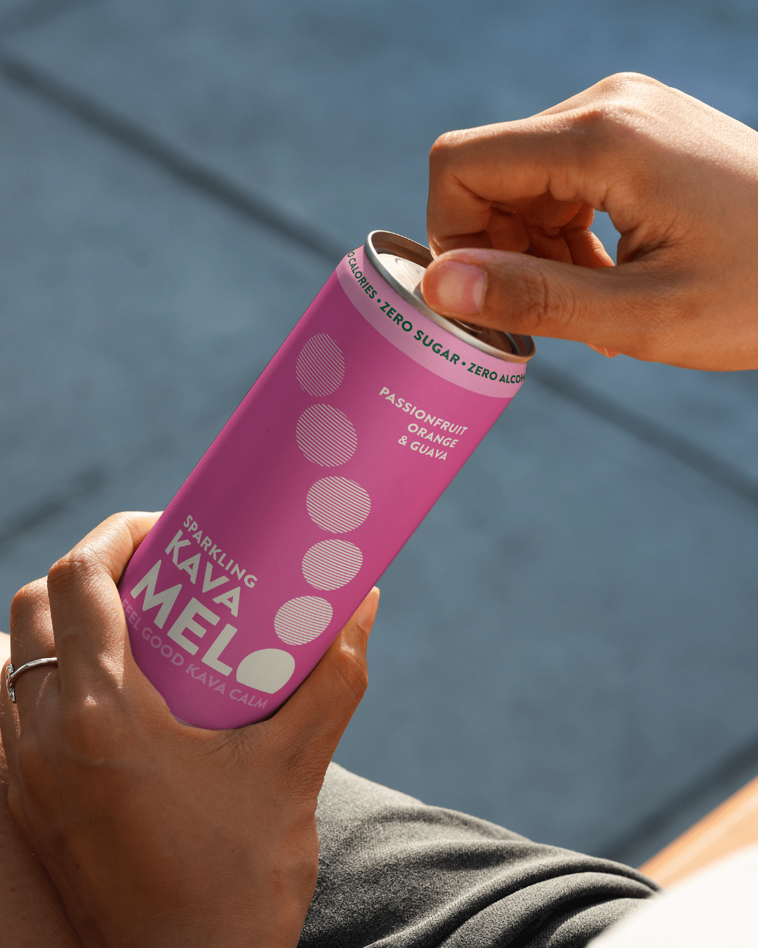 Person holding a pink can of Kava Melo against a blurred background