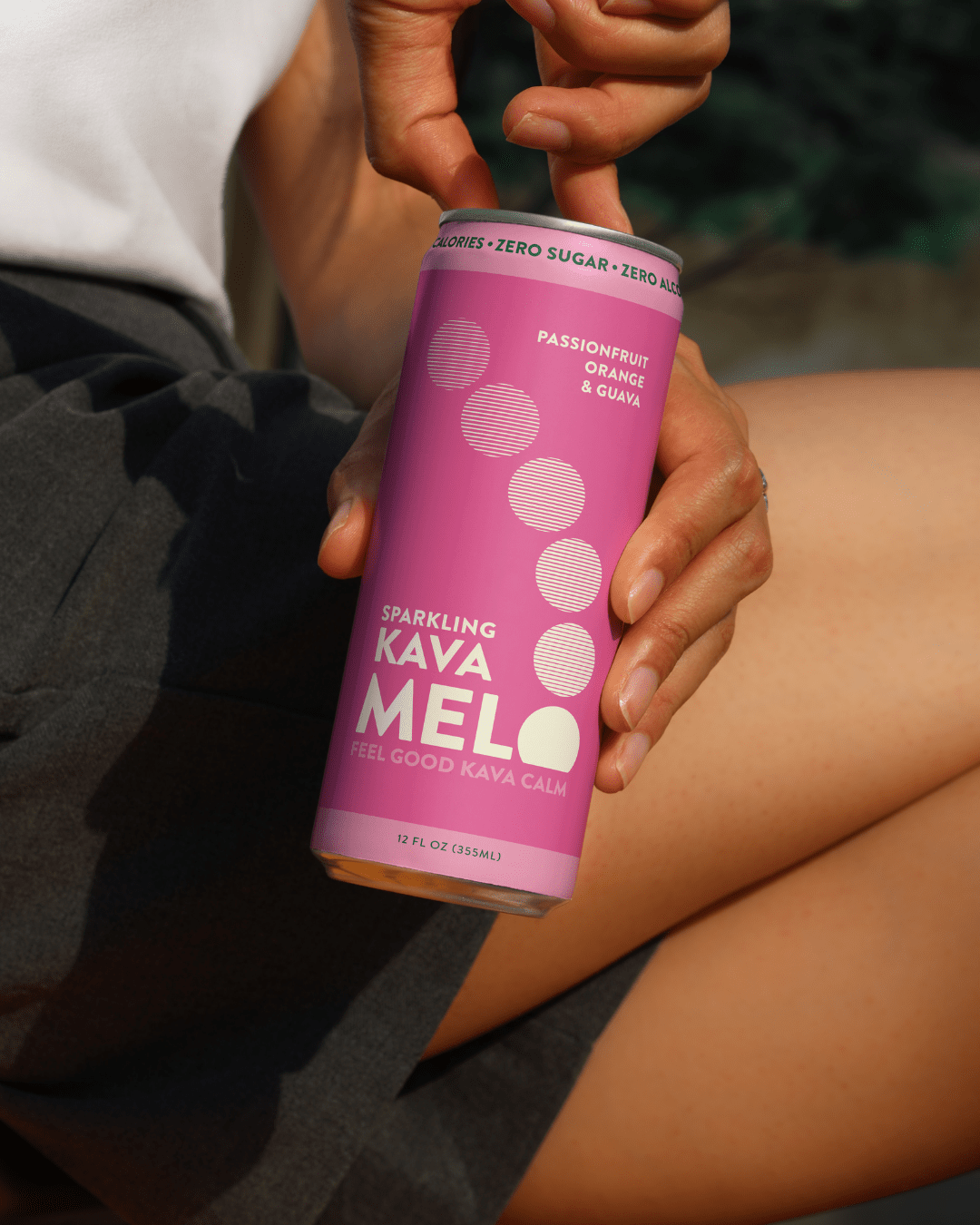 Person holding a pink 'Sparkling Kava Melo' can with a blurred background